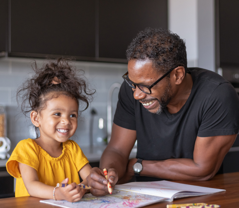 A father coloring with his young daughter at the kitchen table